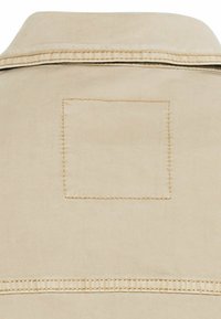 Beige skjorte med krave, et rektangulært syet mærke på ryggen, og en vandret søm ved kanten med synlige stikninger.