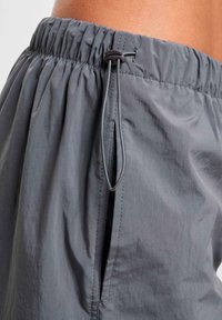 Pantaloni corti leggeri grigi con vita elastica, cordoncino regolabile, tasche laterali e una texture liscia. Progettati per il comfort.