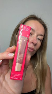 Soin des lèvres Ole Henriksen dans une boîte rose, avec une section transparente dévoilant le produit. Le texte indique « Soin hydratant pour les lèvres » et les ingrédients.