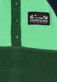 Zeleni flis pulover s tamnozelenim detaljima, sadrži tri crna dugmeta na kopčanje i oznaku "Didriksons". Mekana tekstura i složen dizajn.