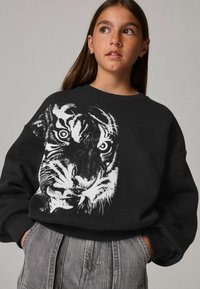 Sudadera negra con un gráfico de un tigre blanco que muestra detalles en el rostro. Cuello redondo, corte relajado y puños acanalados.