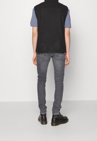 Chaleco de forro polar negro sobre una camiseta azul claro, combinado con jeans grises de corte ajustado y botas de cuero negras con suela marrón.