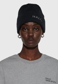 Czarna dziergana czapka z prążkowaną fakturą i wyhaftowanym logo "HALO". Połączona z jasnoszarym swetrem z detalem logo na piersi.