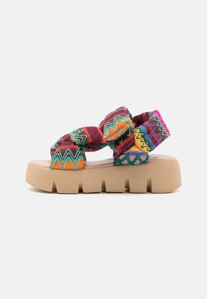 Platform sandal with chunky beige sole and multicolored knitted fabric straps featuring zigzag patterns.