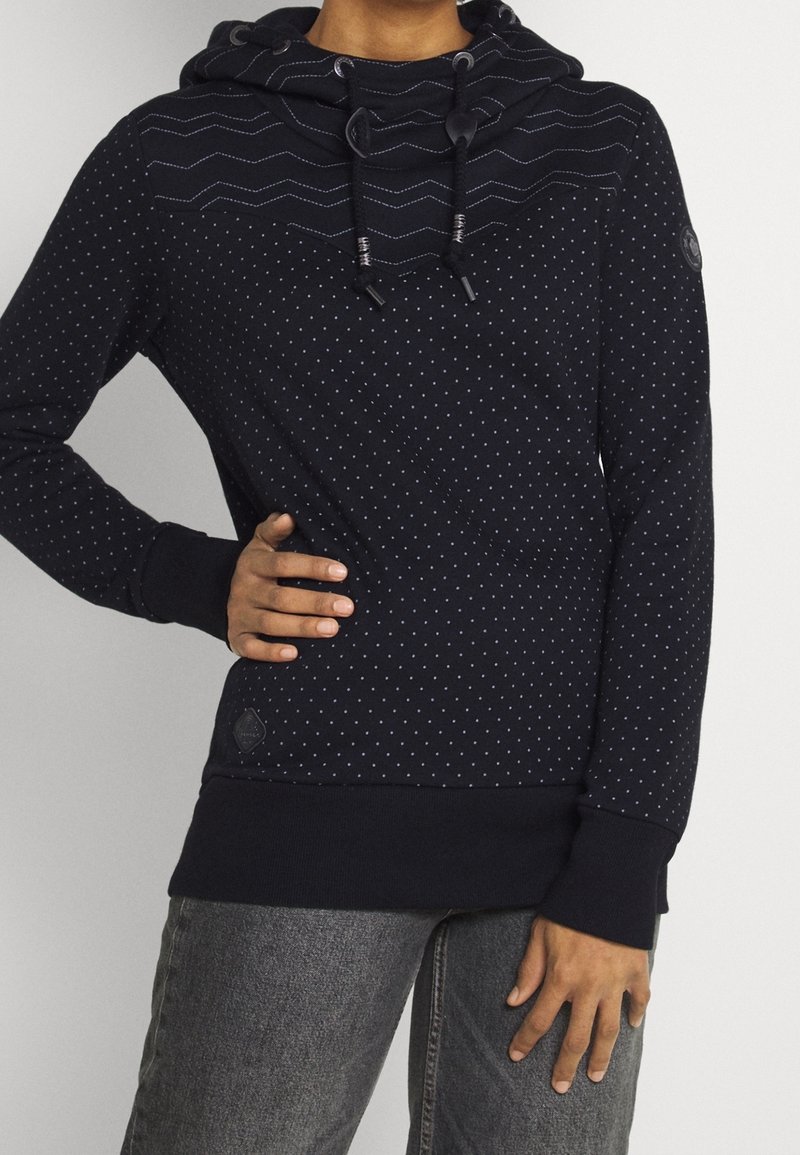 Sudadera azul marino con un diseño de puntos, que presenta un patrón de estilo chevron en el cuello, cordones y puños acanalados. Acentuada con un parche de logo.