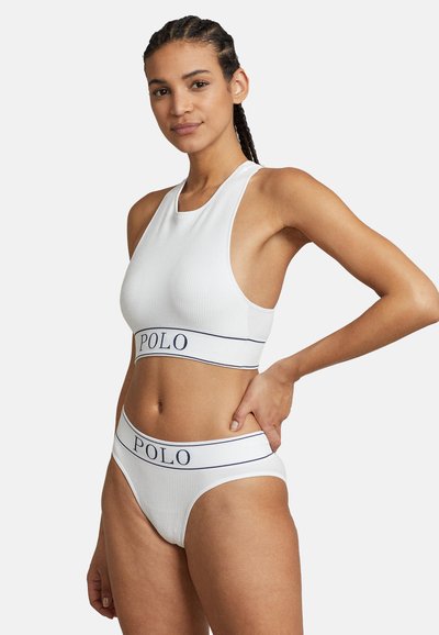 Fehér bordázott cropped top és hozzáillő, magas derekú alsó, melyet egy sötétkék "POLO" logóval díszített pánt jellemez. Sima textúrájú és testhez simuló kialakítású.