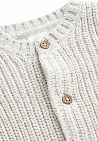 Hellbeige gestrickte Strickjacke mit strukturiertem Muster, Rundhals und Holzknopfverschluss. Das Etikett trägt die Aufschrift "NEXT."