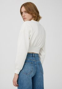 Biały, krótki sweter z bufkami, prążkowanym wykończeniem i gładką fakturą, połączony z niebieskimi dżinsami z wysokim stanem i tylnymi kieszeniami.