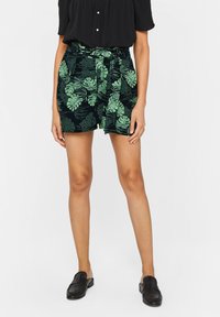 Svarta shorts med ett grönt tropiskt bladmönster, elastisk midja med snörning, måttlig längd, kombinerat med en svart topp och skor.