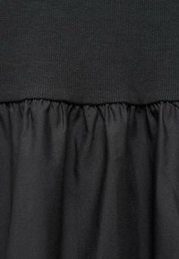 Robe noire avec un haut côtelé et une jupe en tissu lisse et froncé. Le matériau semble doux et tombe à partir d'une taille bien définie.