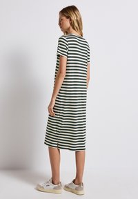 Pasiasta sukienka sięgająca do kolan w ciemnozielonym i kremowym kolorze, wykonana z miękkiego materiału. Posiada krótkie rękawy i boczny rozcięcie. Połączona z białymi trampkami.