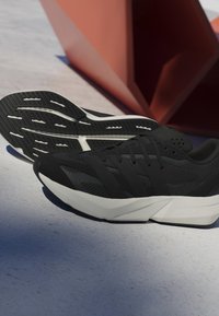 Čierne športové topánky s textúrovaným sieťovinovým zvrškom, s tromi pruhmi a bielou LIGHTSTRIKE strednou podrážkou. Gumová podrážka s protišmykovými vzormi.