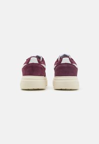 Un paio di sneakers in suede maroon con dettagli bianchi e suole spesse in gomma avorio, viste da dietro su uno sfondo bianco semplice.