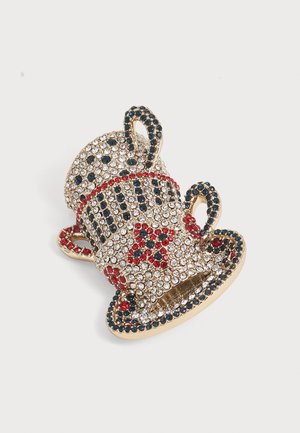 Paire d’épingles en forme de tasse à thé et soucoupe ton or, ornées de strass clairs, rouges et bleu foncé avec des motifs d’étoiles et de rayures.