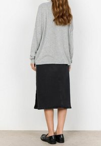 Grå langærmet sweater og sort denimnederdel med sideskår. Flade sorte sko. Blød tekstur, løs pasform og afslappet design.