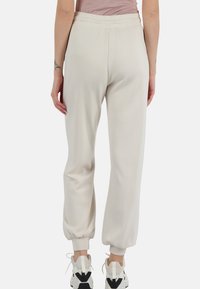 Joggers beige chiaro con vita elastica, gambe affusolate e polsini a coste. Realizzati in tessuto morbido, presentano una texture liscia e una vestibilità casual.