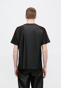 Czarny t-shirt z krótkim rękawem z czerwonymi akcentami na ramionach, okrągły dekolt, gładka faktura i luźny krój. Noszony z ciemnymi, teksturowanymi spodniami.