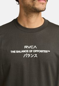 Dunkelgraues Baumwoll-T-Shirt mit Rundhalsausschnitt; mit weißem Text: "RVCA THE BALANCE OF OPPOSITES™ バランス" auf der Vorderseite.