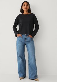 Zwarte langmouwen crop top gecombineerd met lichtblauwe wijde jeans en beige puntige schoenen, met een ontspannen pasvorm en zachte textuur.