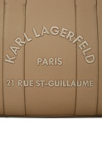 Krémová kožená taška s embosovaným textom: "KARL LAGERFELD PARIS 21 RUE ST-GUILLAUME." Text má tonálny, prešitý dokončenie.