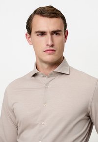 Licht beige overhemd met lange mouwen, een puntige kraag, knopenlijst en een gladde textuur. Een subtiele glans versterkt het verfijnde uiterlijk.