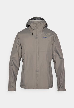 Harmaa vedenpitävä takki hupulla, jossa etuvetoketju, säädettävät kiristysnauhat ja vasemmassa rinnassa logopainatus.