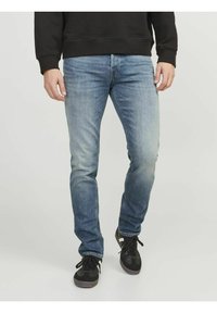 Jean en denim bleu clair avec une coupe slim, présentant un lavage légèrement délavé, un design à cinq poches et des détails de couture subtils. Portés avec des baskets noires.