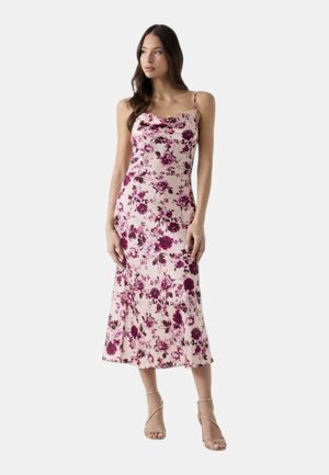 Mujer con un vestido midi sin mangas rosa con estampado floral en tono rosa oscuro y tirantes finos, combinado con sandalias de tacón beige.