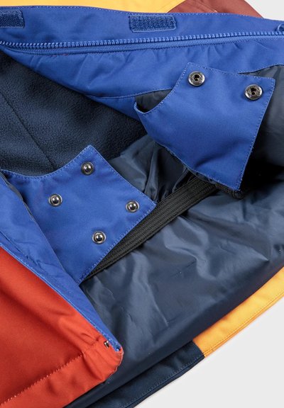 Intérieur coloré d'un sac comprenant des tissus bleu, rouge et orange. Comprend des boutons-pression, des fermetures éclair et un doublure en polaire bleu texturé.