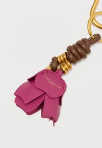 Ādas atslēgu piekariņš ar rozā ziedlapiņām, brūniem spirāļiem un zelta akcentiem. Ar tekstūru, kurā redzami šuvumi un zīmols.