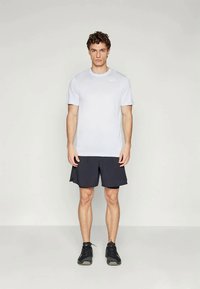 Maglietta sportiva bianca a maniche corte con un piccolo logo, abbinata a pantaloncini scuri e scarpe da corsa nere. Design semplice, materiale leggero.