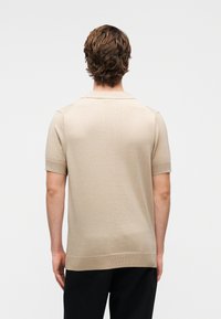 Μπεζ πλεκτό πόλο μπλουζάκι με κοντά μανίκια, με επίπεδη λαιμόκοψη και ριμπ τελειώματα. Λείο ύφασμα και απλός σχεδιασμός, χωρίς ορατά σχέδια.