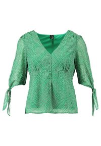 Blouse verte avec col en V, manches bouffantes et détails à nouer. Présente un motif géométrique et une texture légère et transparente.