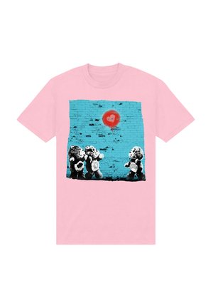 Lyserød t-shirt med et grafisk print af tre bamser foran en turkis murstenvæg med et rødt hjerte symbol over dem.