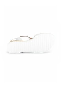 Sandale blanche pour femmes avec une semelle plate et striée, un design à bout ouvert et plusieurs lanières. La partie supérieure a une finition brillante avec des accents marron.