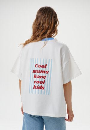Persoon met lang golvend haar, die een wit t-shirt draagt met blauwe strepen en rode tekst ""Cool mums have cool kids"" op de rug.