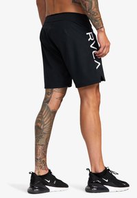 Sorte boardshorts med hvid "RVCA"-logo på siden, der har en afslappet pasform og letvægtsmateriale. Teksturiserede tatoveringer synlige på benet.