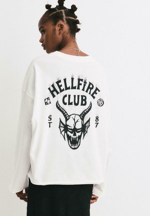 Weißer Langarm-Sweatshirt mit einem schwarzen grafischen Design eines Schädels mit Hörnern und dem Text "HELLFIRE CLUB" auf der Rückseite.