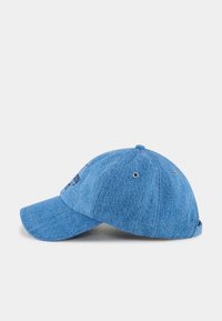 Blå denimbasebollkeps med en krökt skärm, platta sömmar, justerbart band, broderade detaljer och ventilationshål.