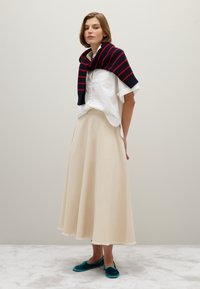 Beige cotton skirt with fringe hem, white button-up shirt, and navy striped knit sweater draped over shoulders. Teal slippers complete the outfit.
