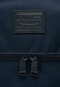 Námořnický látkový batoh s obdélníkovou koženou nášivkou s vyraženým logem značky, dvojími černými zipy s designem hor.