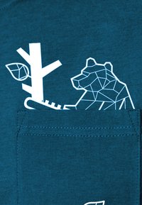 Türkisfarbenes Baumwoll-T-Shirt mit einem weißen geometrischen Bären- und Baumdesign im Bereich der Brusttasche, mit glatter Textur und einfacher Naht.