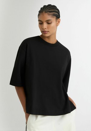 Czarny oversize'owy t-shirt wykonany z bawełny, z okrągłym dekoltem, krótkimi rękawami i luźnym krojem, o gładkiej fakturze.