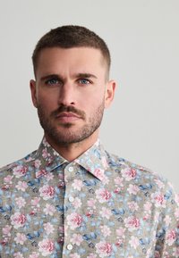 Bloemenprint overhemd met korte mouwen in beige stof, met roze en blauwe bloemenmotieven, een klassieke kraag en witte knopen.