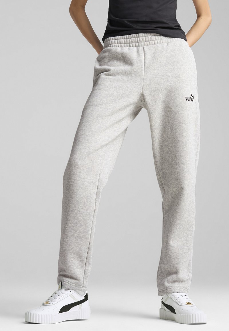 Grå sweatpants gjorda av mjukt tyg, med resårmidja och sidofickor. Svart Puma-logotyp på vänster sida. Matchas med vita sneakers.