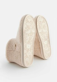 Chausson en feutre de couleur rose clair avec une semelle en caoutchouc texturée présentant un motif géométrique et une ventilation latérale discrète. Matériau doux et confortable.