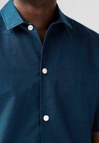 Camicia corta navy realizzata in tessuto leggero, con colletto button-down, taschino frontale e bottoni bianchi in contrasto.