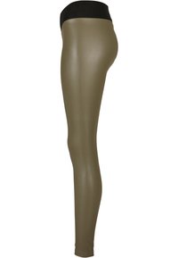 Vista laterale di una persona che indossa leggings a vita alta di colore verde oliva con una fascia nera su uno sfondo bianco.