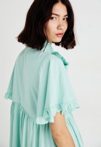 Vestido verde menta con mangas acampanadas y diseño acampanado. Fabricado en una tela ligera, tiene una silueta fluida y un corte relajado.