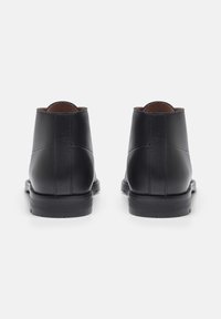 Bottes de cheville en cuir noir avec une finition lisse, bout rond et petit talon empilé. Présente des coutures minimales et une silhouette classique.